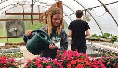 young girl in green house watering flowers